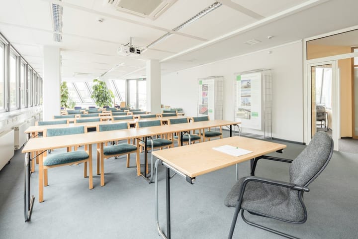 A classroom with tables facing a the front of the room and a single desk and chair in front. 