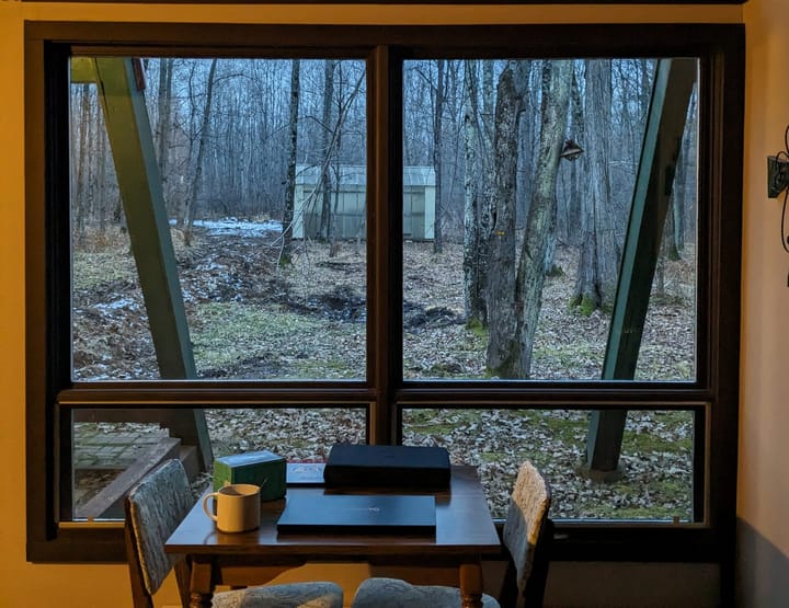 A small table in front of a window overlooking a winter forest scene. 